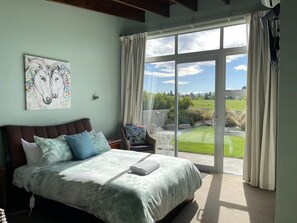 Un dormitorio con una cama grande, una silla y vistas a un jardín a través de un ventanal corredero.