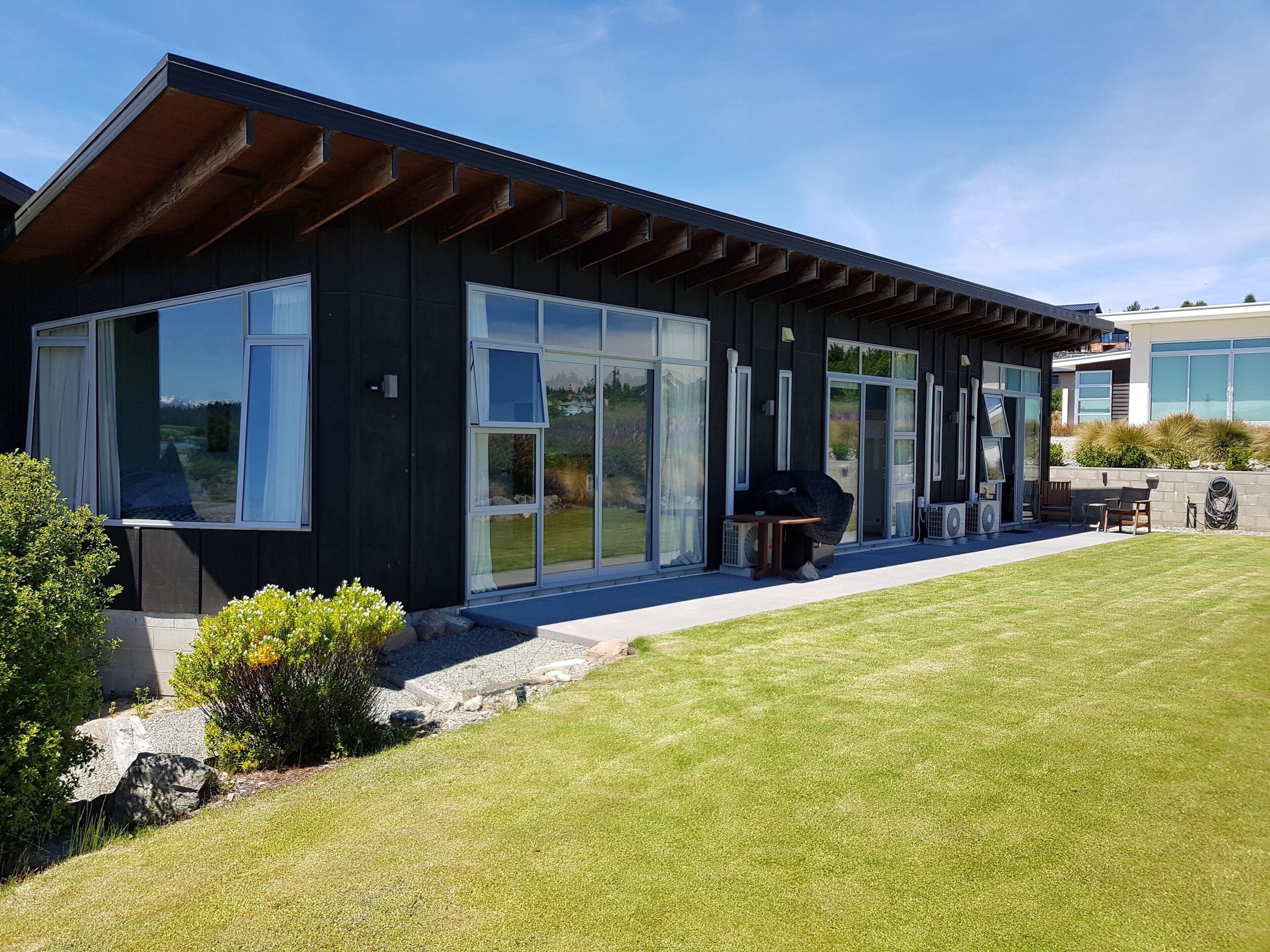 A modern house with large sliding glass doors, a covered patio, and a well-maintained lawn.