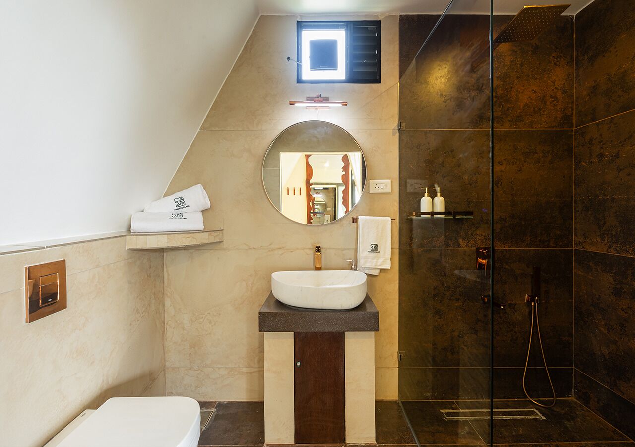 A modern bathroom with a large mirror, a round sink, a shower, and a small window.