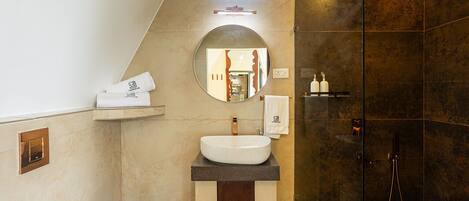 A modern bathroom with a large mirror, a round sink, a shower, and a small window.