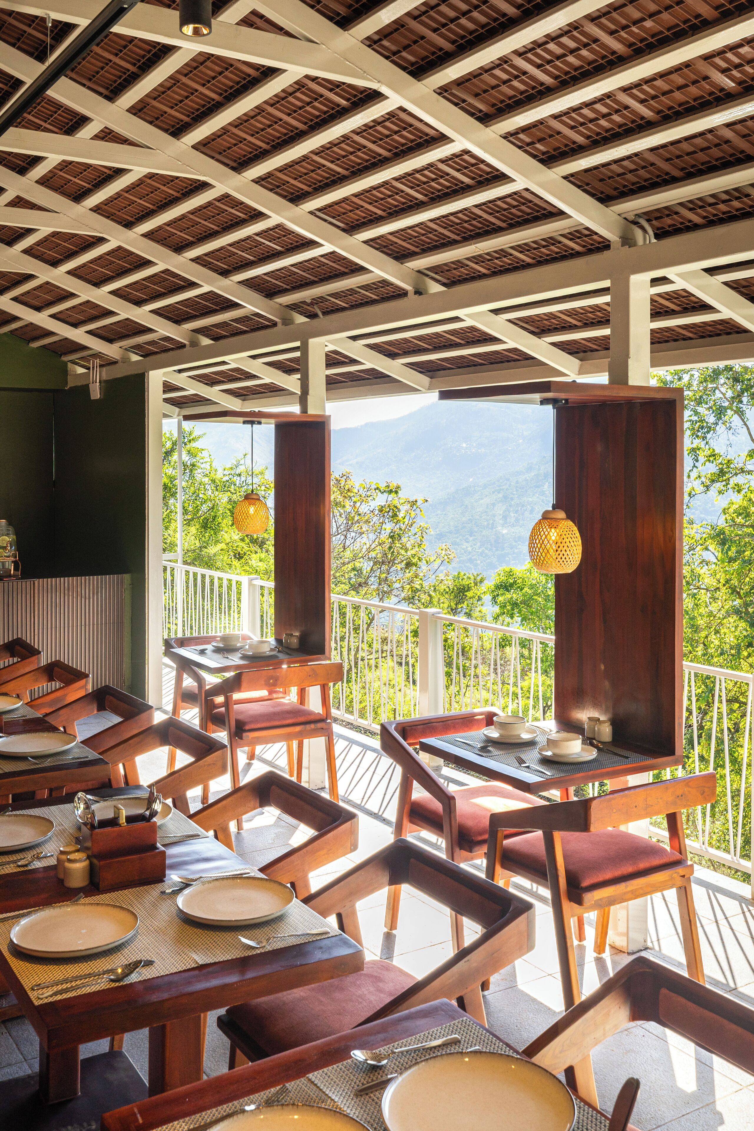 A dining area with tables and chairs, a wooden ceiling, and a view of greenery and mountains.