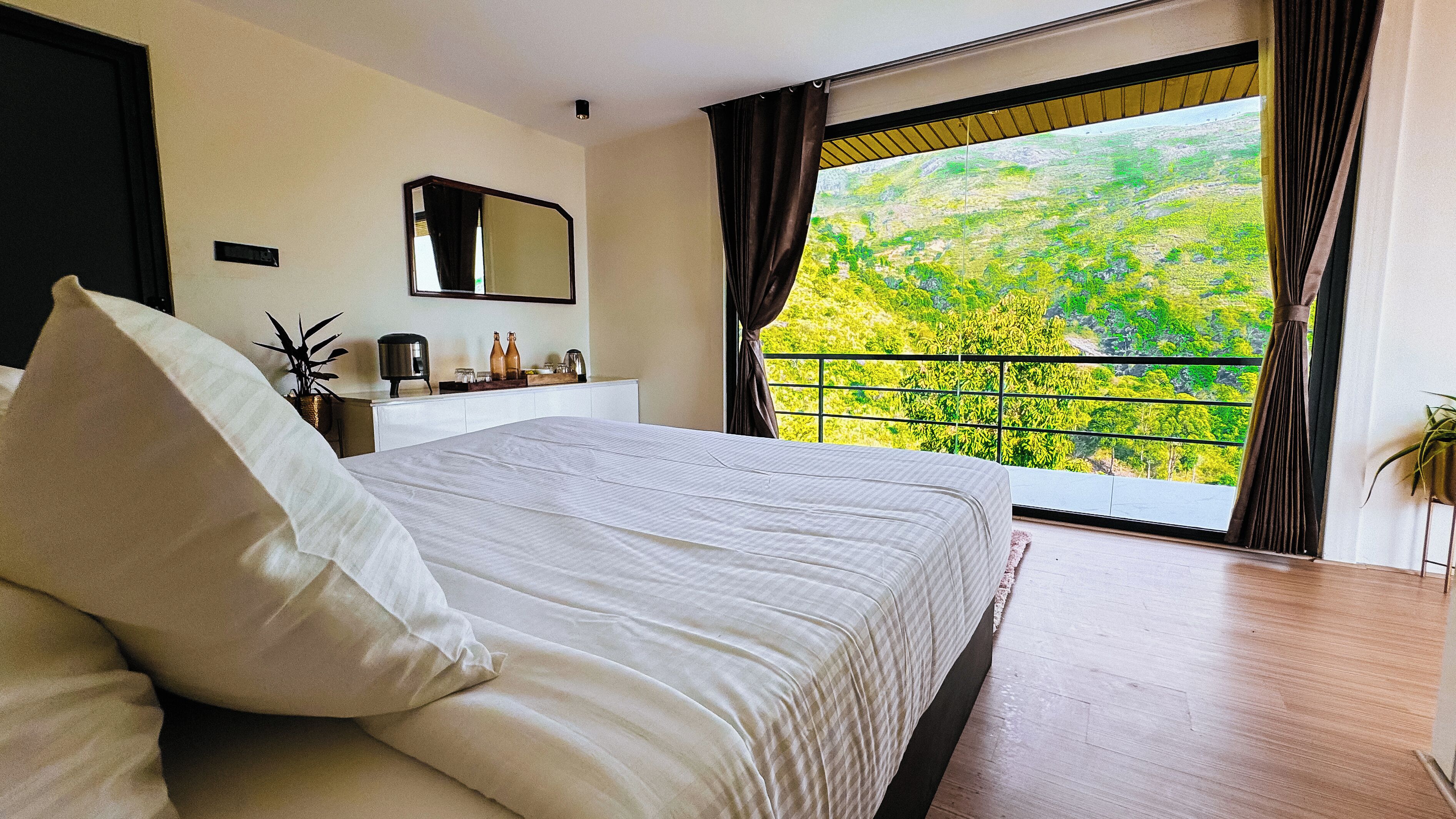 Un dormitorio con una cama grande, un aparador, un espejo y un balcón con vistas a la vegetación.