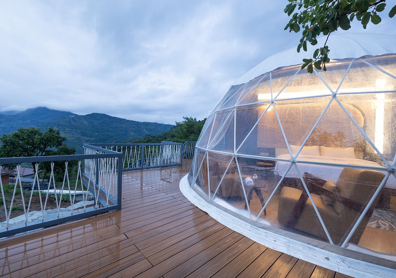 A dome-shaped structure with a transparent roof on a wooden deck, overlooking a mountainous landscape.