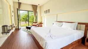 A hotel room with a large bed, a wooden floor, a dining table with chairs, and a view of greenery through the window. - TOMORROWLAND  FARMS AND SUITES (Kodaikanal)