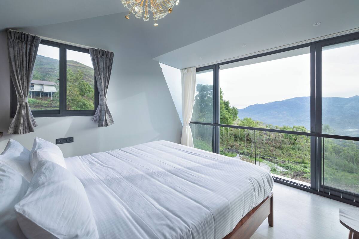 Quarto com cama grande, duas janelas e vista para o exterior.