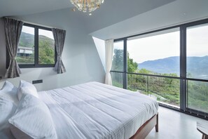 A bedroom with a large bed, two windows, and a view of the outdoors. - TOMORROWLAND  FARMS AND SUITES (Kodaikanal)