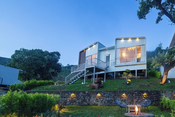 A modern house with a staircase leading to a deck, surrounded by greenery and a stone wall with outdoor seating. - TOMORROWLAND  FARMS AND SUITES (Kodaikanal)