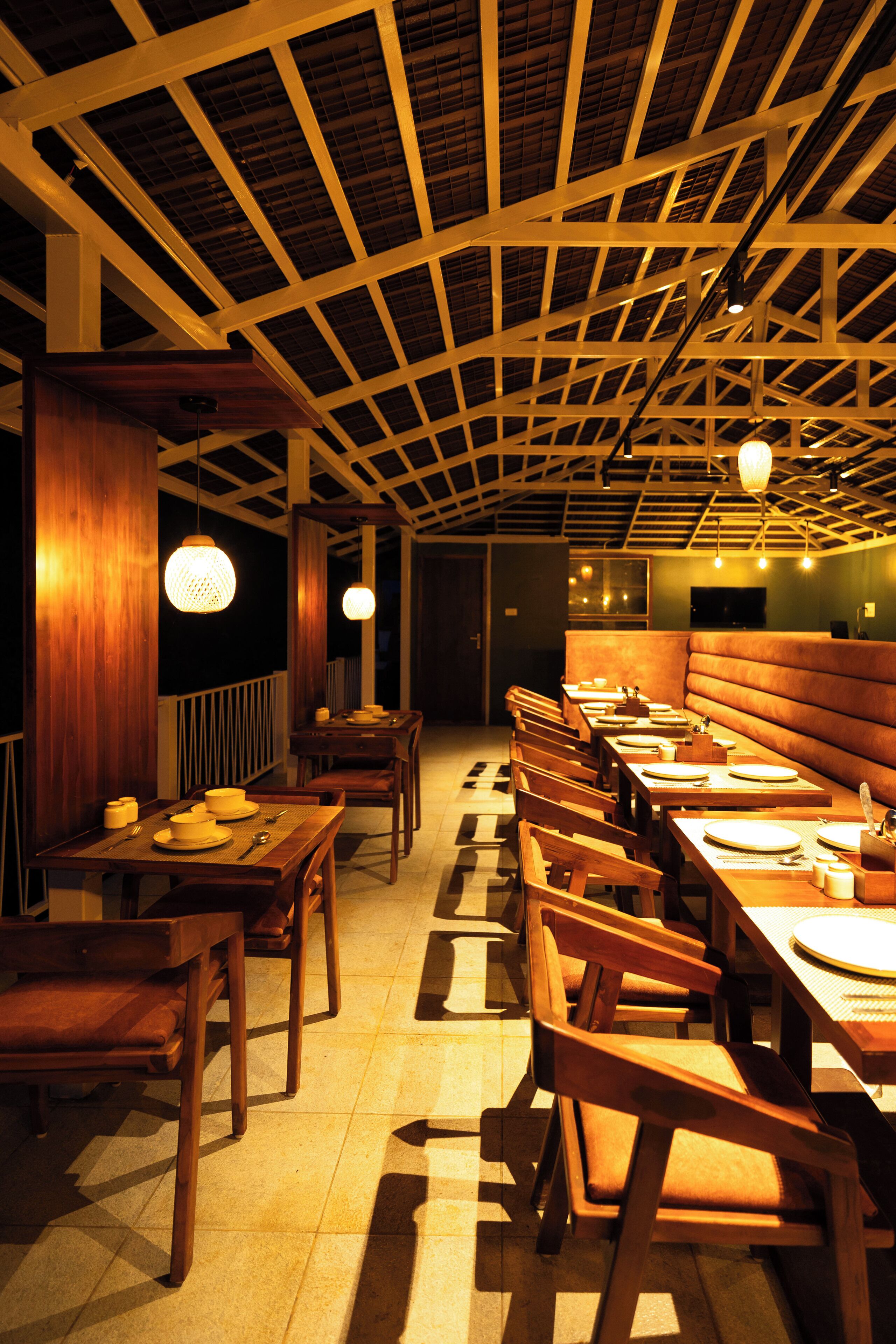 A restaurant with wooden tables and chairs, a high ceiling with a grid pattern, and pendant lighting.