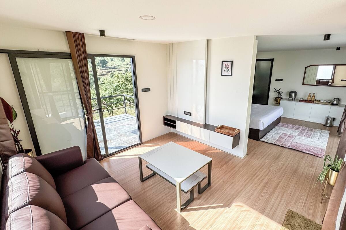 Uma sala de estar moderna com um sofá, uma mesa de centro e uma porta de vidro deslizante que dá para uma varanda.