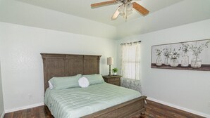 A bedroom with a wooden bed, a nightstand with a lamp, a ceiling fan, and a floral painting on the wall. - 4 Bedroom, 2 Bath in Midlothian! Centrally Located, Pet Friendly, Close to Local Wedding Venues. (Midlothian)