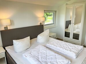 A neatly made bed with white bedding, a bedside table with a lamp, a window with a view of greenery, and a wardrobe with mirrored doors. - Geesthof by Interhome (Hechthausen)