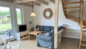 A modern living room with a wooden staircase, a grey sofa, a wooden coffee table, and a TV on a white stand.