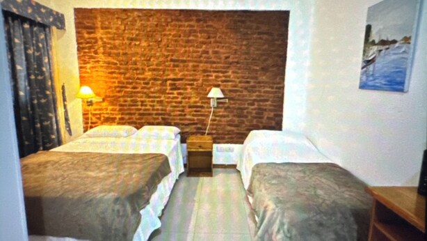 A room with two beds, a brick wall, a painting, and a lamp. - Departamento Obelisco (Buenos Aires)