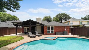 A backyard with a swimming pool, a covered patio with seating, and a brick house. - Near Stadiums, Epic Central, Featuring a Private Pool (Grand Prairie)