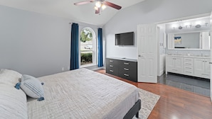 A bedroom with a bed, a ceiling fan, a dresser, a TV, and a bathroom with a sink and mirror. - Near Stadiums, Epic Central, Featuring a Private Pool (Grand Prairie)