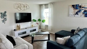 A modern living room with a flat-screen TV, a glass coffee table, a dark sofa, and a white entertainment unit.