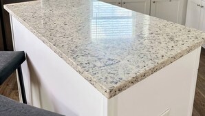 A modern kitchen with white cabinetry, a granite countertop, and a stainless steel refrigerator.
