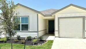 A single-story house with a garage, a front door, and a small front yard with a tree and shrubs.