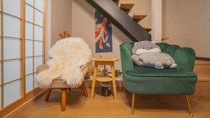 A room with a green armchair, a fluffy chair, a small wooden stool, and a staircase. - Miyu Bonichi (Osaka)