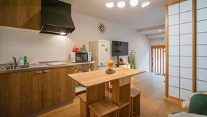 A modern kitchen with wooden cabinets, a microwave, and a sink. There is a small table with a decorative item on it. - Miyu Bonichi (Osaka)