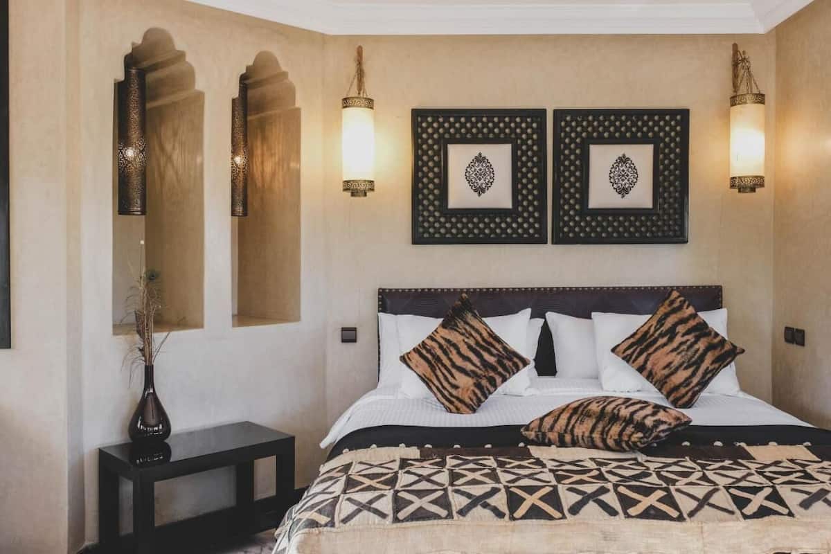 Une chambre d’hôtel avec un lit, deux lampes fixées au mur et deux tableaux encadrés.