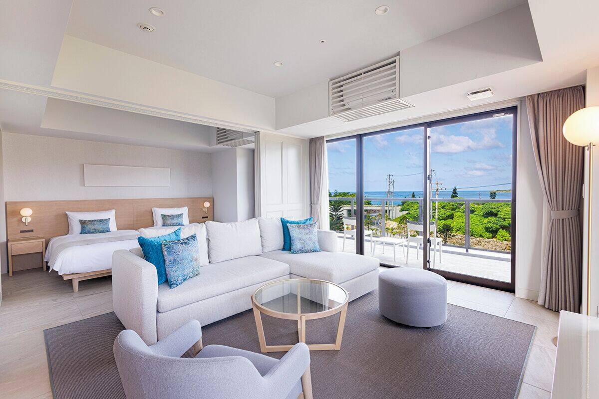 Une chambre d’hôtel moderne dotée d’un grand lit, d’un canapé, d’une table basse en verre et offrant une vue sur la mer.