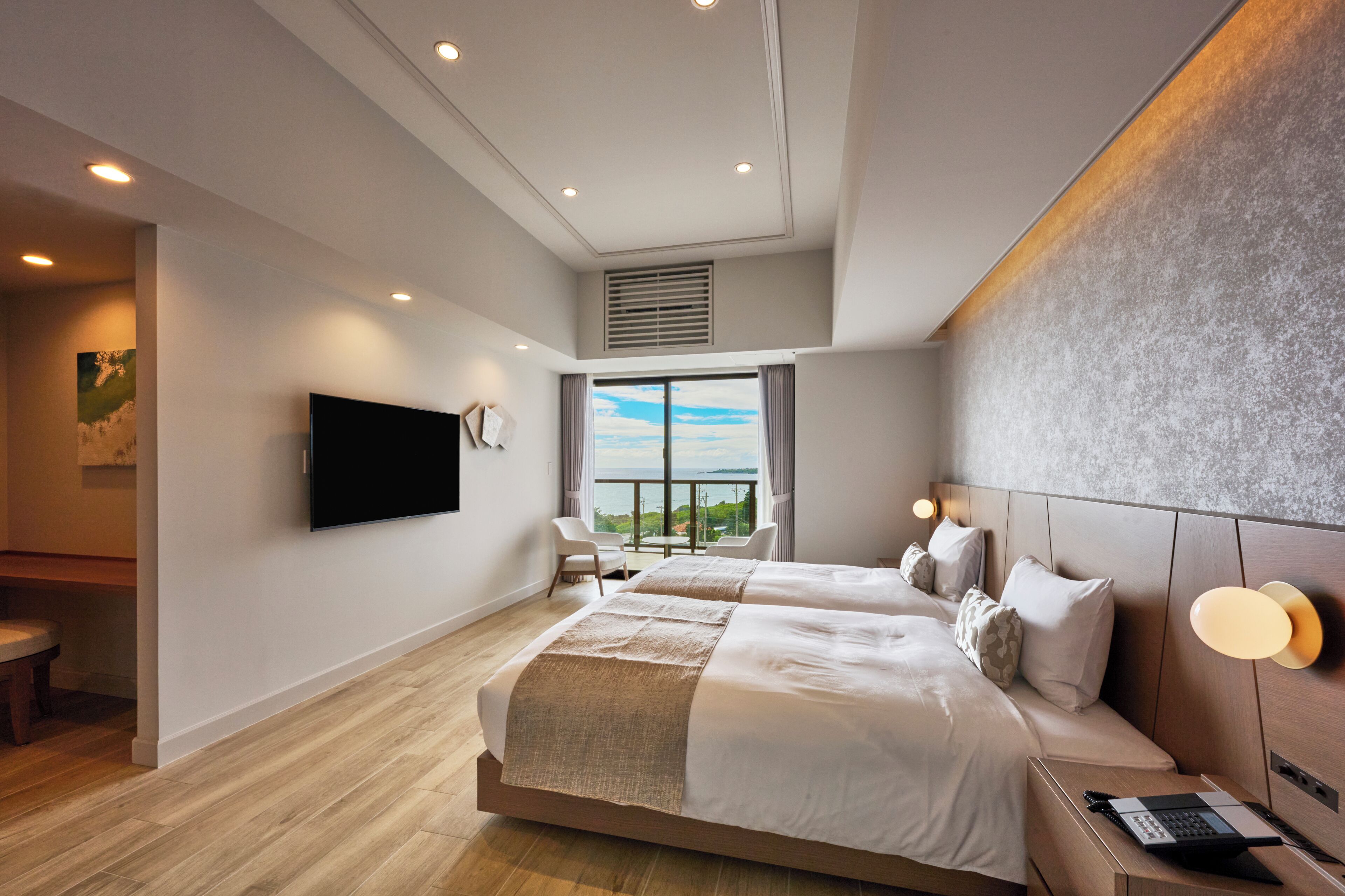 Een moderne hotelkamer met twee bedden, een flatscreen-tv, een balkon met uitzicht en een bureau met lamp.