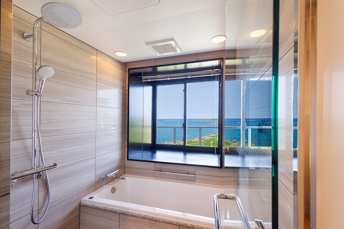 Un baño moderno con bañera, ducha y ventanas amplias con vistas al mar.