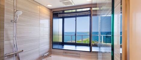 Un baño moderno con bañera, ducha y ventanas amplias con vistas al mar.