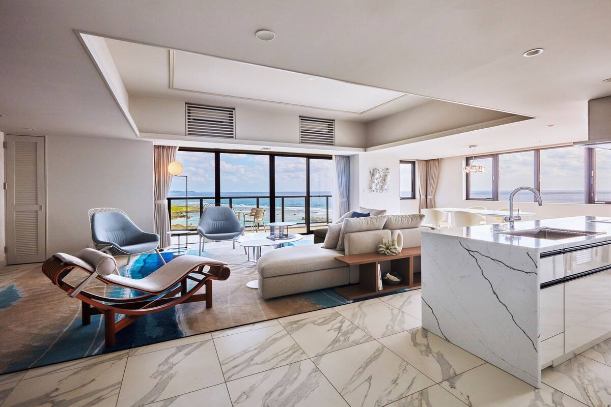 Un espace de vie moderne avec vue sur la mer, un sol en marbre et une cuisine dotée d’un îlot central en marbre.