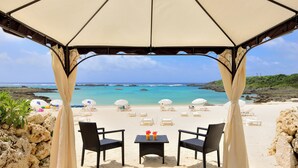 A beachside seating area with a table, two chairs, and a canopy overlooking the ocean. - Hotel Shigira Mirage Beach Front (Miyakojima)