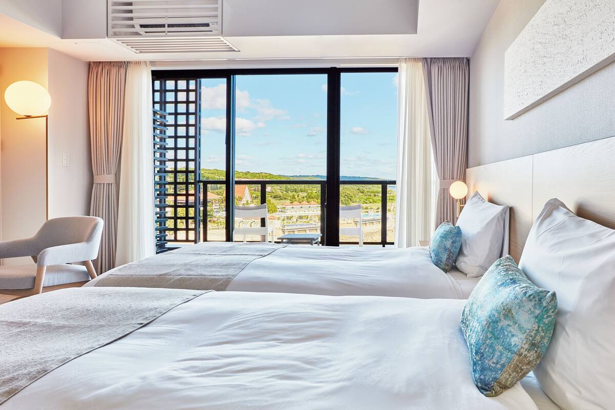 Une chambre d’hôtel avec un grand lit, une chaise et une vue sur un balcon aménagé avec du mobilier d’extérieur.
