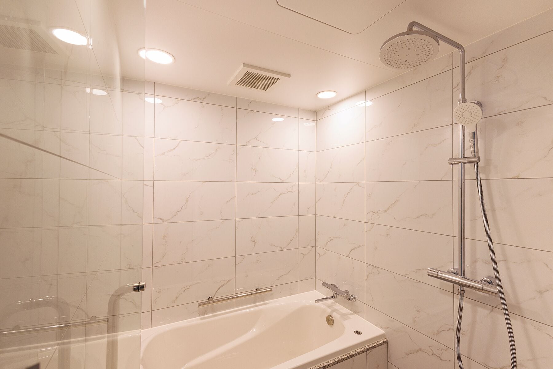 Une salle de bain moderne équipée d’une baignoire, d’une douche avec un pommeau de douche amovible et d’un panneau de commande fixé au mur.