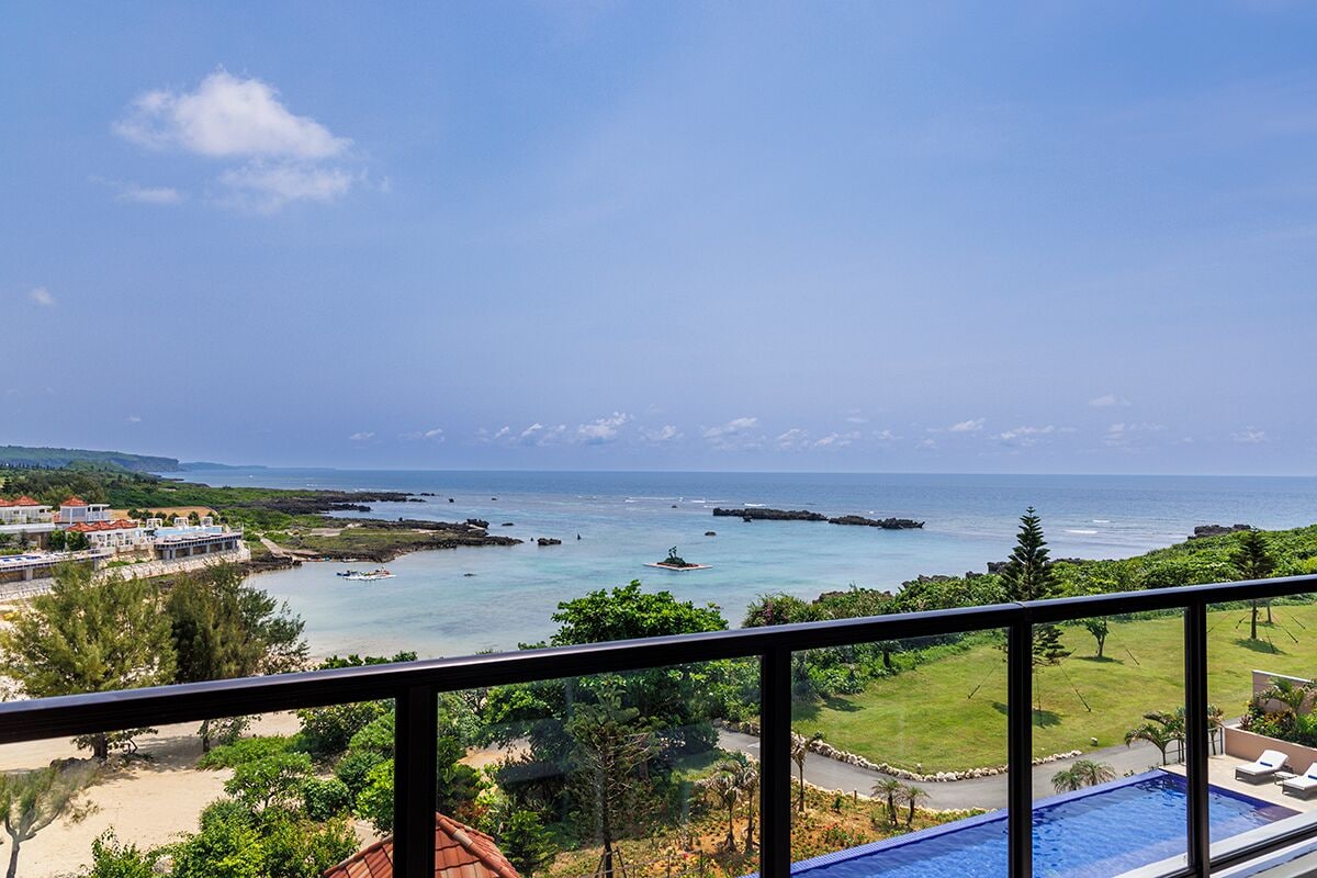 Un balcon offrant une vue sur une plage, l’océan et des montagnes lointaines.