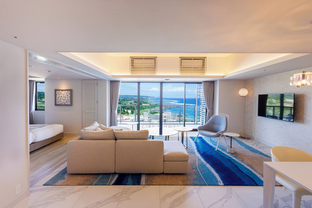 Une chambre d’hôtel moderne dotée d’une grande fenêtre, d’un canapé, d’une table à manger et d’un téléviseur.