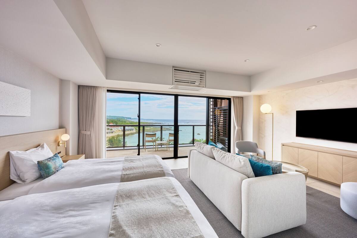 Une chambre d’hôtel moderne avec deux lits, un canapé, une télévision et un balcon offrant une vue agréable.