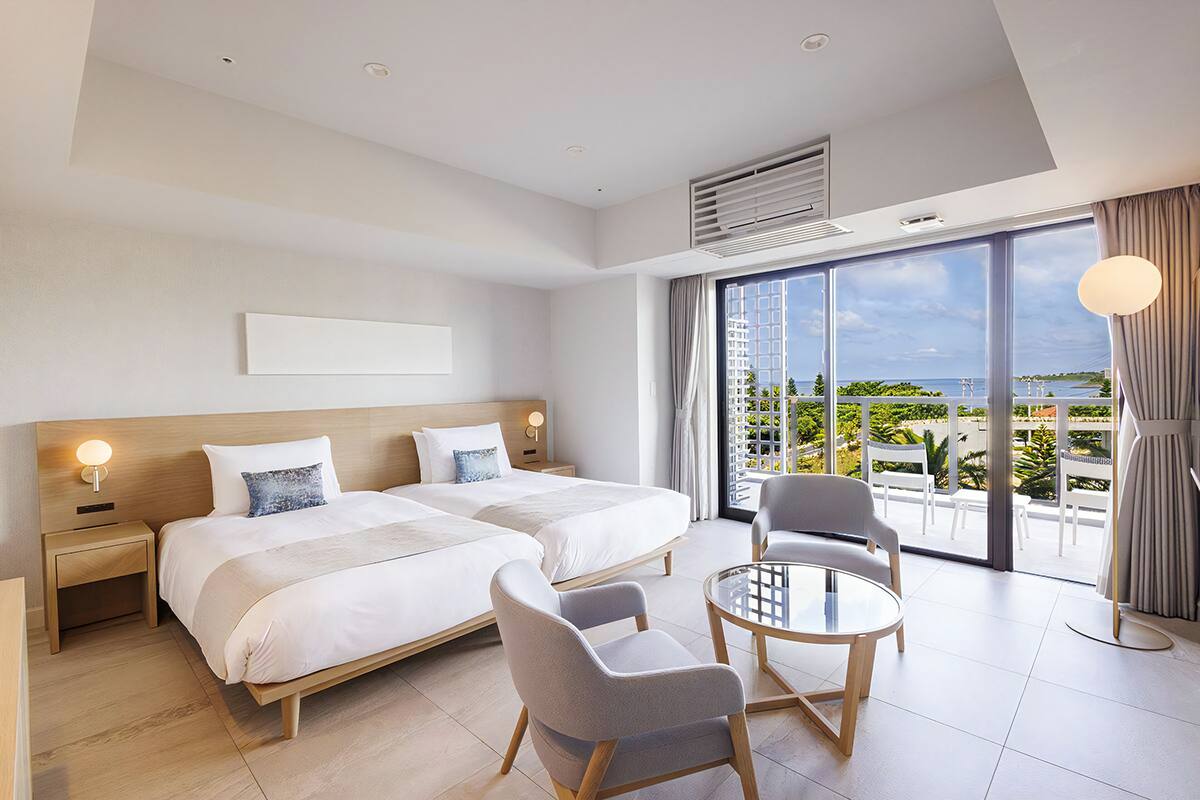 Une chambre d’hôtel avec deux lits, un balcon offrant une vue agréable et une petite table ronde avec des chaises.