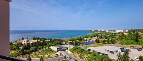 A coastal view from a balcony overlooking a parking lot, a road, and a bridge leading to a beach.