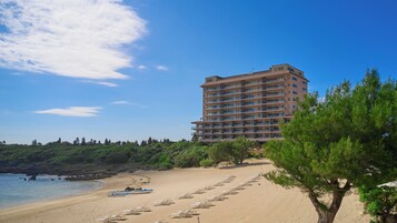 A beachfront hotel with a sandy beach, rows of sun loungers, and a row of boats.