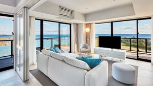 A modern living room with a large sofa, a television, and a view of the ocean. - Hotel Shigira Mirage Beach Front (Miyakojima)