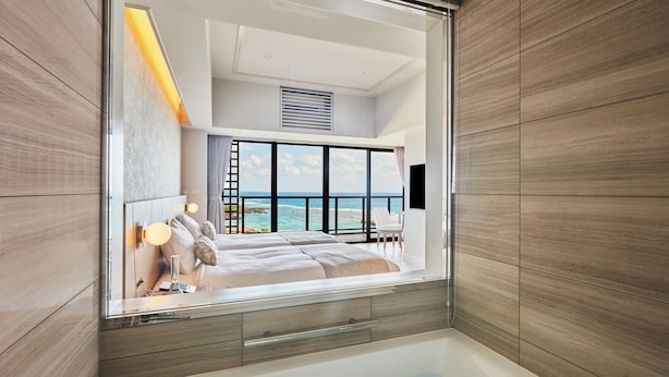 A modern bathroom with a large bathtub, a shower area, and a view of the ocean through large windows. - Hotel Shigira Mirage Beach Front (Miyakojima)