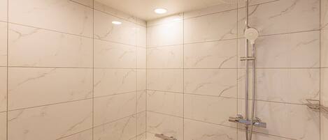 A bathroom with a bathtub, a shower with a handheld showerhead, and a wall-mounted toilet.