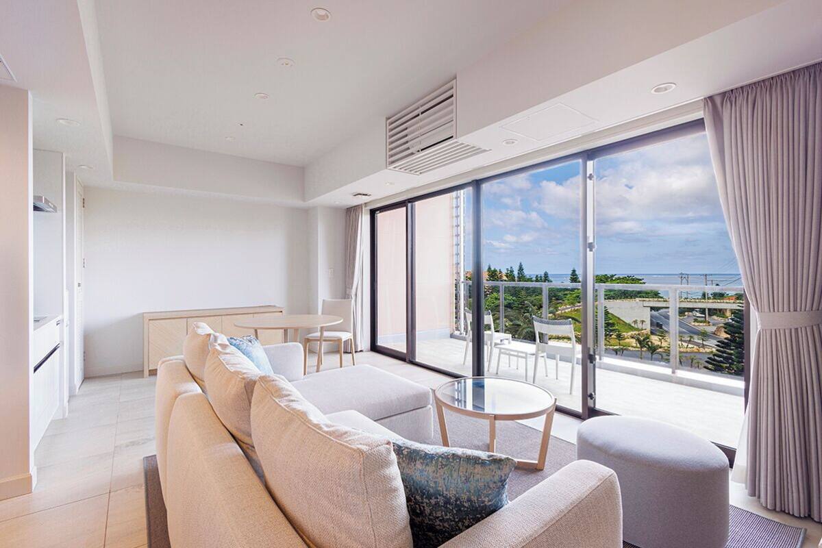 Un salon moderne avec un canapé, une table ronde et une vue sur la mer grâce à de grandes fenêtres.