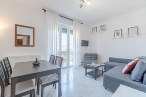 Una sala de estar moderna con una mesa de comedor, sillas, un sofá, una mesa baja, un televisor y un balcón con cortinas.