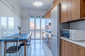Una cocina con mesa, sillas, refrigerador, microondas y vistas a través de puertas de vidrio.