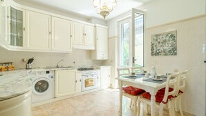 A kitchen with white cabinets, a washing machine, a stove, and a dining area with a table and chairs. - Colle Degli Ometti Vintage Chic Flat x5 (Genova)
