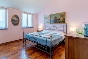 Une chambre à coucher avec un lit en métal, un plancher en bois, un tableau au-dessus du lit et une fenêtre avec des rideaux.