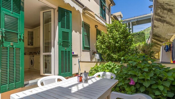 A patio with a table and chairs, a washing machine, and a garden with green foliage. - Colle Degli Ometti Vintage Chic Flat x5 (Genova)