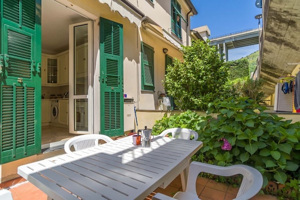 A patio with a table and chairs, a washing machine, and a garden with green foliage.