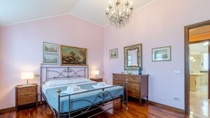A bedroom with a metal bed frame, two bedside tables with lamps, a wooden dresser, and a mirror. - Colle Degli Ometti Vintage Chic Flat x5 (Genova)